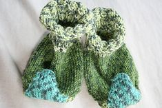 a pair of green and blue knitted baby booties on a white sheet,