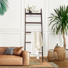 a living room with a leather couch, potted plant and ladder in the corner