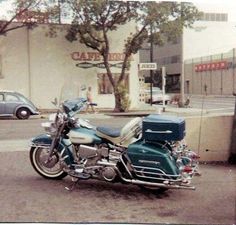 a blue motorcycle parked in front of a building on the side of a road with cars behind it