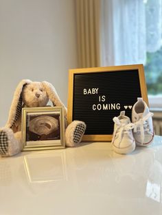 a teddy bear sitting next to a baby's coming sign and shoes on a table