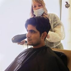 a man getting his hair cut by a woman with a mask over her face and another person in the background