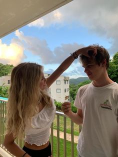 a man standing next to a woman on top of a balcony near a lush green field