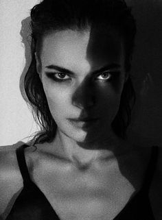 black and white photograph of a woman with blue eyes looking at the camera while standing in front of a wall