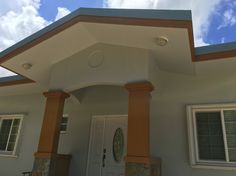 a white house with two windows and an orange trim on the front door is under a cloudy blue sky