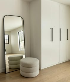 a large mirror sitting on top of a wooden floor next to a white cabinet and ottoman