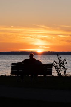 a man sitting on top of a bench next to the ocean at sunset or dawn