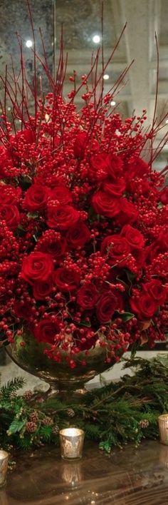 a vase filled with red roses and greenery on top of a table next to candles