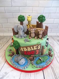 a green cake with animals and trees on it's top, sitting on a wooden table