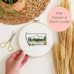 a hand embroidery pattern with the outline of a lake and mountains on it, surrounded by wheat stalks