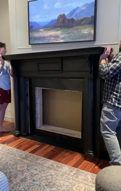 two people are standing in front of a fireplace with a painting on the wall behind them