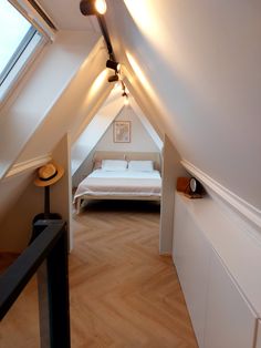 an attic bedroom with white walls and wood flooring is seen from the hallway to the bed