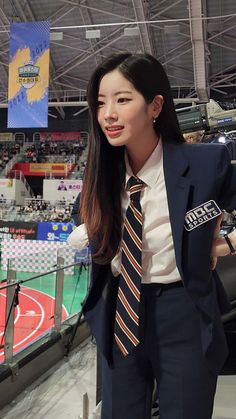 a woman wearing a suit and tie standing in front of an empty basketball court at a sporting event