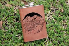 a flask with a drawing of mountains and trees on it sitting in the grass