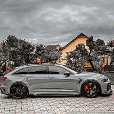 a grey car parked in front of a house on a cobblestone street with trees