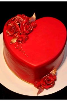 a red heart shaped cake with roses on it's side and gold trimmings