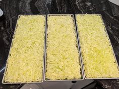 three pans filled with shredded cheese sitting on top of a black marble countertop