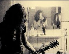 a woman with long hair playing an electric guitar in a bathroom next to a sink