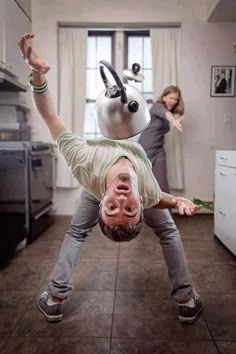 a man upside down in the kitchen with a teapot on his head and hands