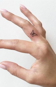 a person's hand with a small butterfly tattoo on the middle of their finger