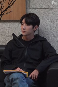 a young man sitting in a chair holding a book and looking off to the side