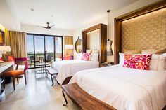 a hotel room with two beds, desk and large sliding glass doors leading to the balcony