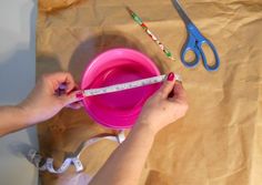 a woman measuring her pink bowl with a tape measure and scissors on the table next to it