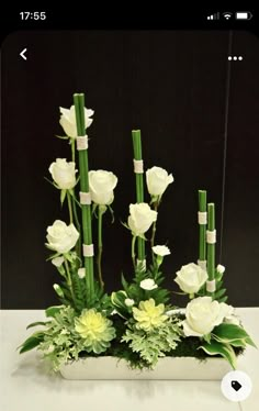 white flowers and greenery are arranged in a square vase with bamboo sticks sticking out of it