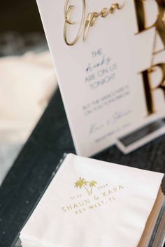 an open book sitting on top of a table next to a white napkin and gold foil lettering