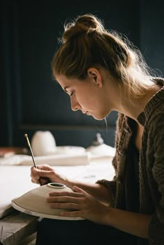 a woman sitting at a table writing on a piece of paper with a pen in her hand