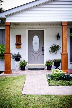 the front door of a white house with potted plants and flowers on either side