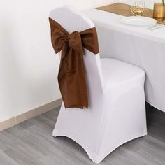 a white chair with a brown bow tied to it's back sitting in front of a table