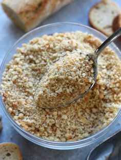 a spoon full of bread crumbs in a glass bowl with slices of bread on the side