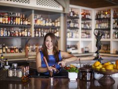 a woman standing at the bar with a cocktail in her hand and holding a shaker