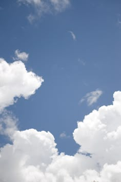 an airplane is flying high in the sky with white clouds behind it and trees below