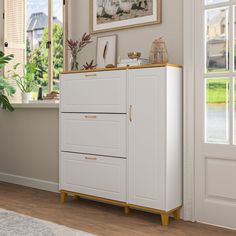 a white cabinet with gold handles next to a window and potted plant in the corner