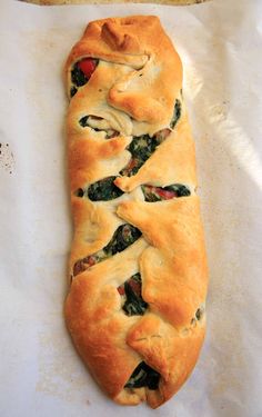 a piece of bread with spinach and cheese on it sitting on top of parchment paper