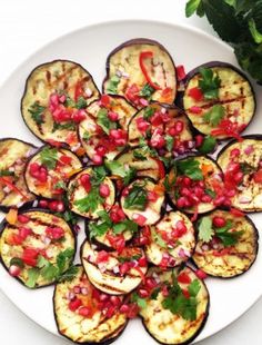 a white plate topped with grilled eggplant slices covered in pomegranate