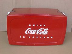 an old coca - cola cooler is sitting on the floor