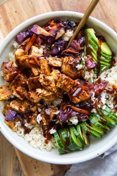 a bowl filled with rice, meat and vegetables on top of a wooden cutting board