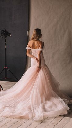 a woman in a pink wedding dress standing on a wooden floor next to a camera