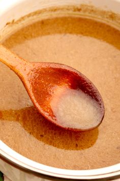 a wooden spoon in a bowl filled with brown liquid and white flecks on top