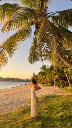 a woman standing on top of a lush green field under a palm tree next to the ocean