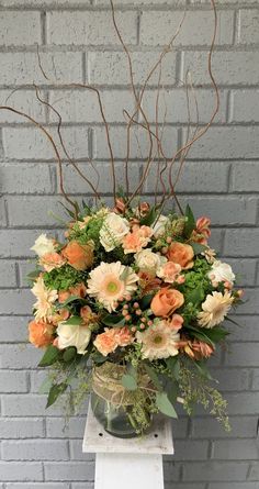 a vase filled with lots of flowers on top of a white pedestal next to a brick wall