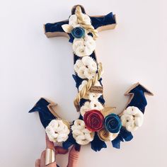 a hand holding a cross made out of fabric flowers and ribbon with the letter e on it