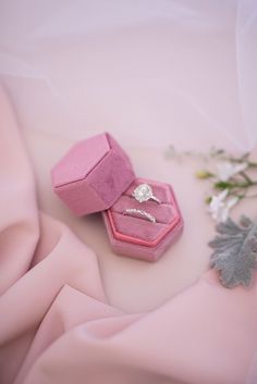 two wedding rings in pink velvet boxes on a satin table cloth with flowers and leaves