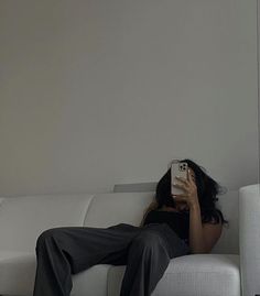 a woman sitting on top of a white couch holding a cell phone up to her face