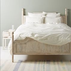 a bed with white sheets and pillows in a room next to a rug on the floor