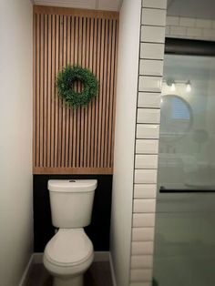 a white toilet sitting in a bathroom next to a wooden paneled wall with a wreath on it