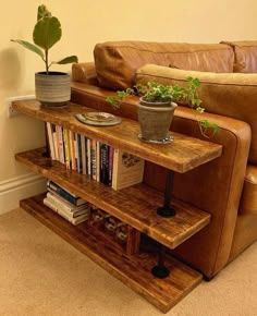 a brown couch sitting next to a wooden shelf filled with books and potted plants