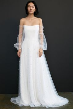 a woman in a white wedding dress standing against a black wall with her hands on her hips